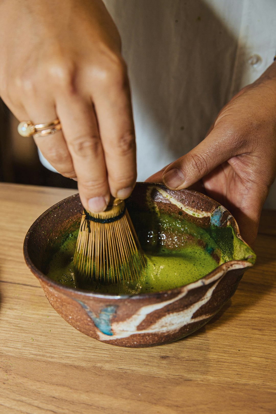 Woman preparing matcha with a bamboo whisk in natural light
